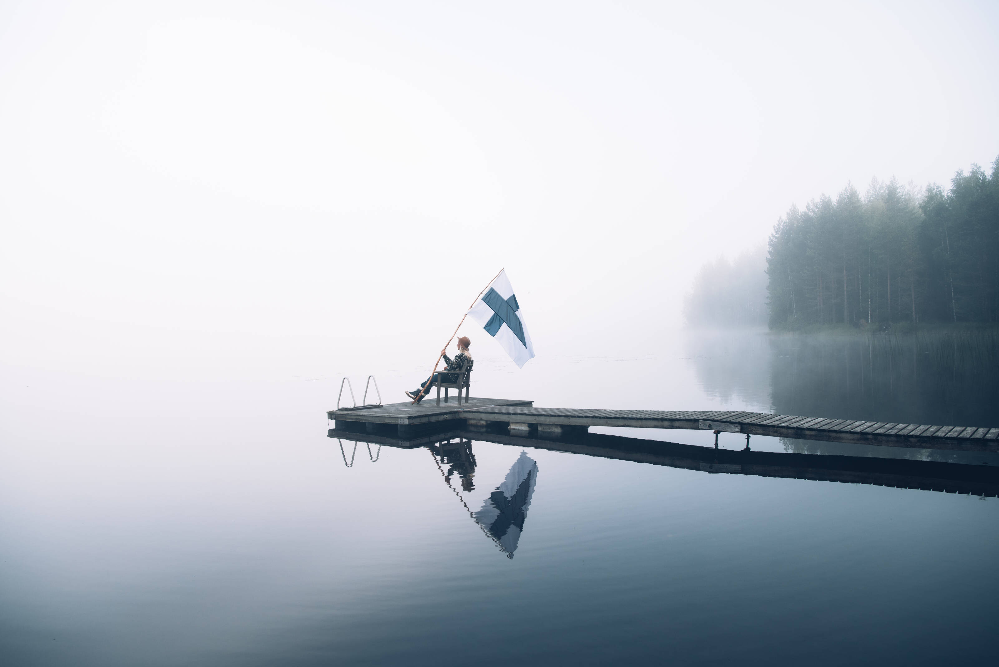 Person sitting at a lake with the Finnish flag.